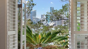 A view from a window with a cityscape in the background, including a distinctive building with a white facade and a tree in the foreground. - Harbourfront Haven –4BR Retreat with Stunning Views of Sydney’s Iconic La... (Cremorne Point)