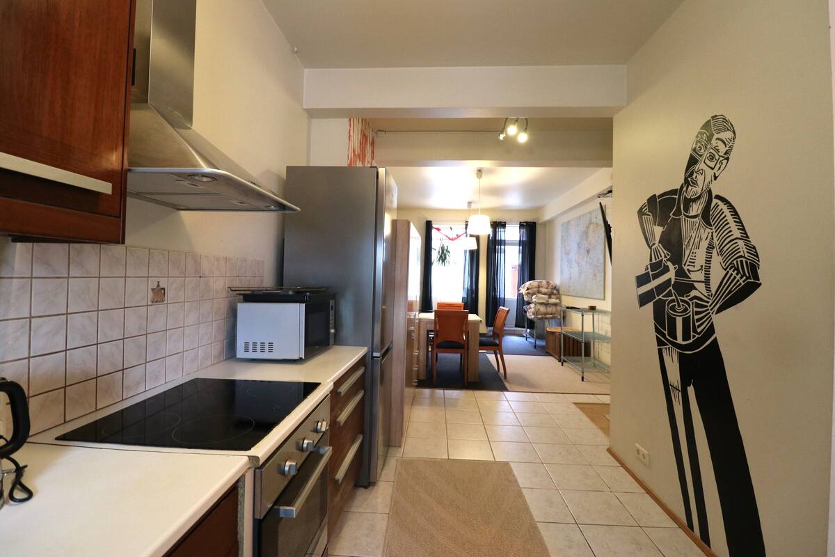 A modern kitchen with a built-in stove, refrigerator, and microwave. There is a dining area with a table and chairs visible in the background.
