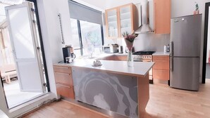 A modern kitchen with wooden cabinets, a stainless steel refrigerator, and a large window providing natural light. - Antique Rentals (Reykjavik)