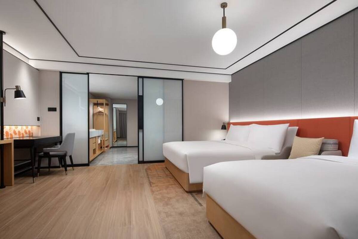 Ein modernes Hotelzimmer mit zwei Betten, einem Schreibtisch und einem Sessel.