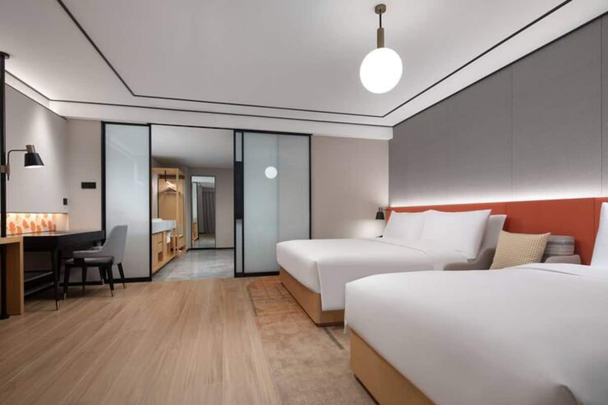 Ein modernes Hotelzimmer mit zwei Betten, einem Schreibtisch und einem Sessel.