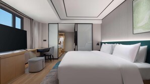A modern hotel room with a large bed, a desk with a flat-screen TV, a seating area with a chair, and a walk-in closet. - Hilton Garden Inn Chengde Mountain Resort (Chengde)