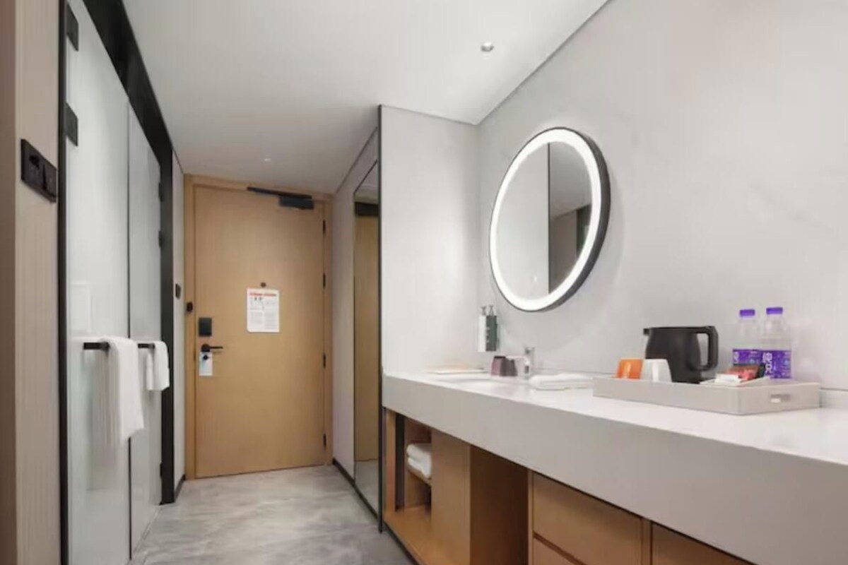 Un baño moderno con un espejo grande, un lavamanos y una encimera con artículos de aseo.