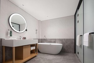 A modern bathroom with a freestanding bathtub, a round mirror with a light, and a vanity with a wooden cabinet.
