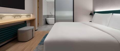 Un hotel moderno con una cama grande, un tocador con espejo, una bañera y vista al mar a través de una puerta de cristal.