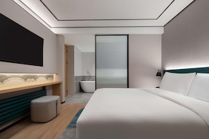 Un hotel moderno con una cama grande, un tocador con espejo, una bañera y vista al mar a través de una puerta de cristal.