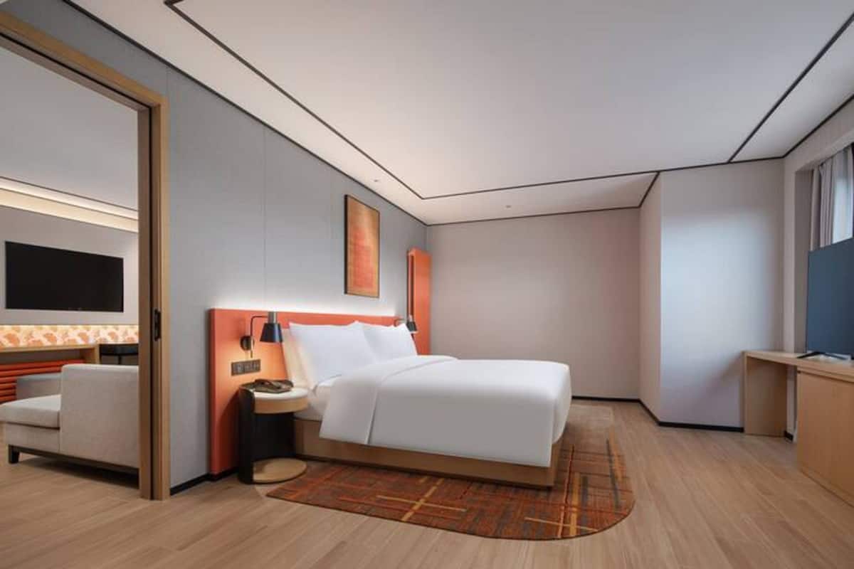Ein modernes Hotelzimmer mit einem großen Bett, einem Schreibtisch, einem Sessel und einem Fernseher.