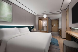 A hotel room with a large bed, a desk, a chair, a wardrobe, and a television.