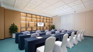 A conference room with multiple tables, white chairs, and a large screen displaying the Hilton Garden Inn logo.