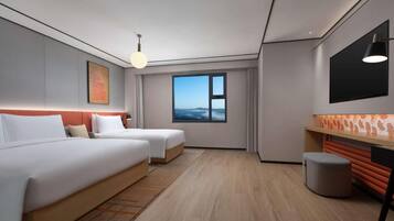 A modern hotel room with two beds, a large window, and a view of the sky.