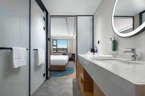 A modern hotel room with a large bed, a bathroom with a double sink and a large mirror, and a view of the city through the window. - Hilton Garden Inn Chengde Mountain Resort (Chengde)