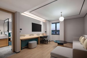 Una habitación de hotel moderna con cama, escritorio, silla, una mesita pequeña y un gran ventanal.