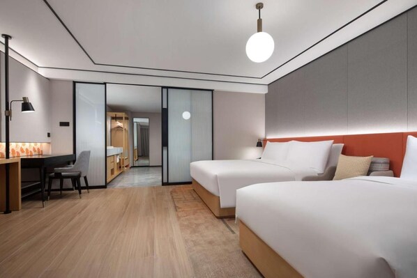 A modern hotel room with two beds, a desk, and a chair.