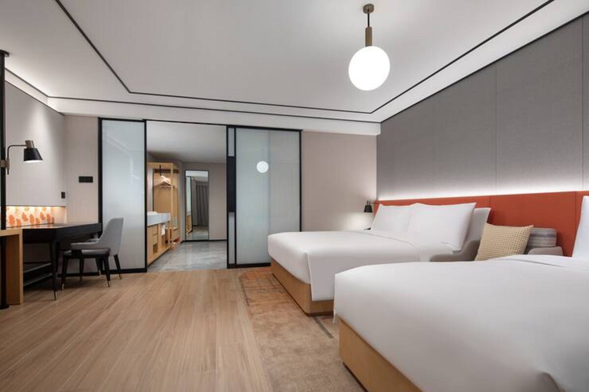 A modern hotel room with two beds, a desk, and a chair.