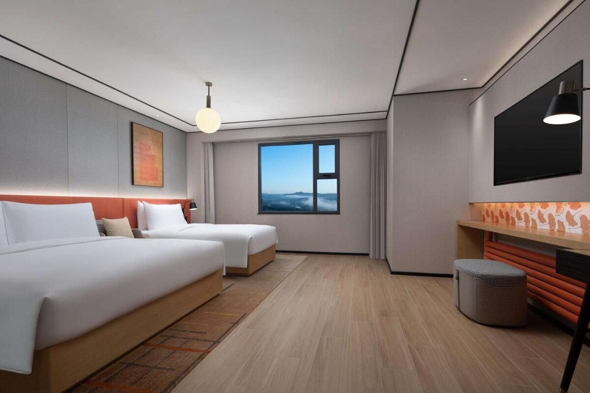 A modern hotel room with two beds, a large window, and a view of the sky.