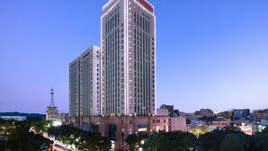 A high-rise hotel with a prominent red logo on the top, surrounded by other buildings and trees. - Hilton Garden Inn Chengde Mountain Resort (Chengde)