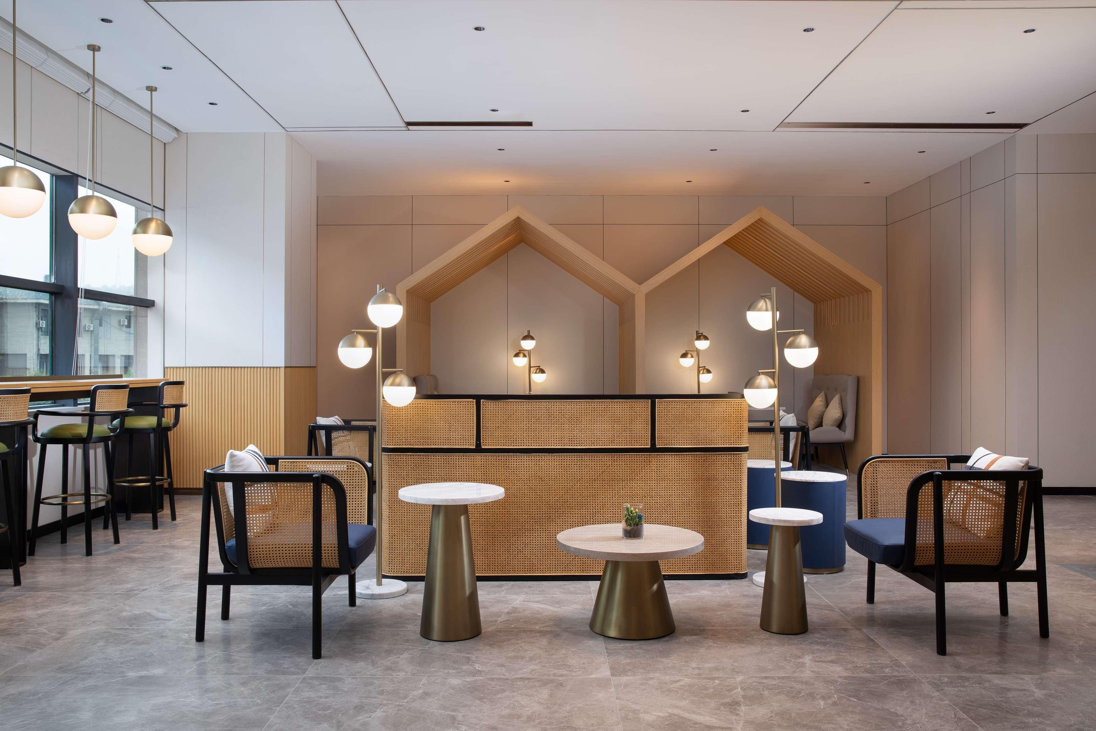 Een moderne receptie met een houten receptiebalie, ronde tafels en rieten stoelen.