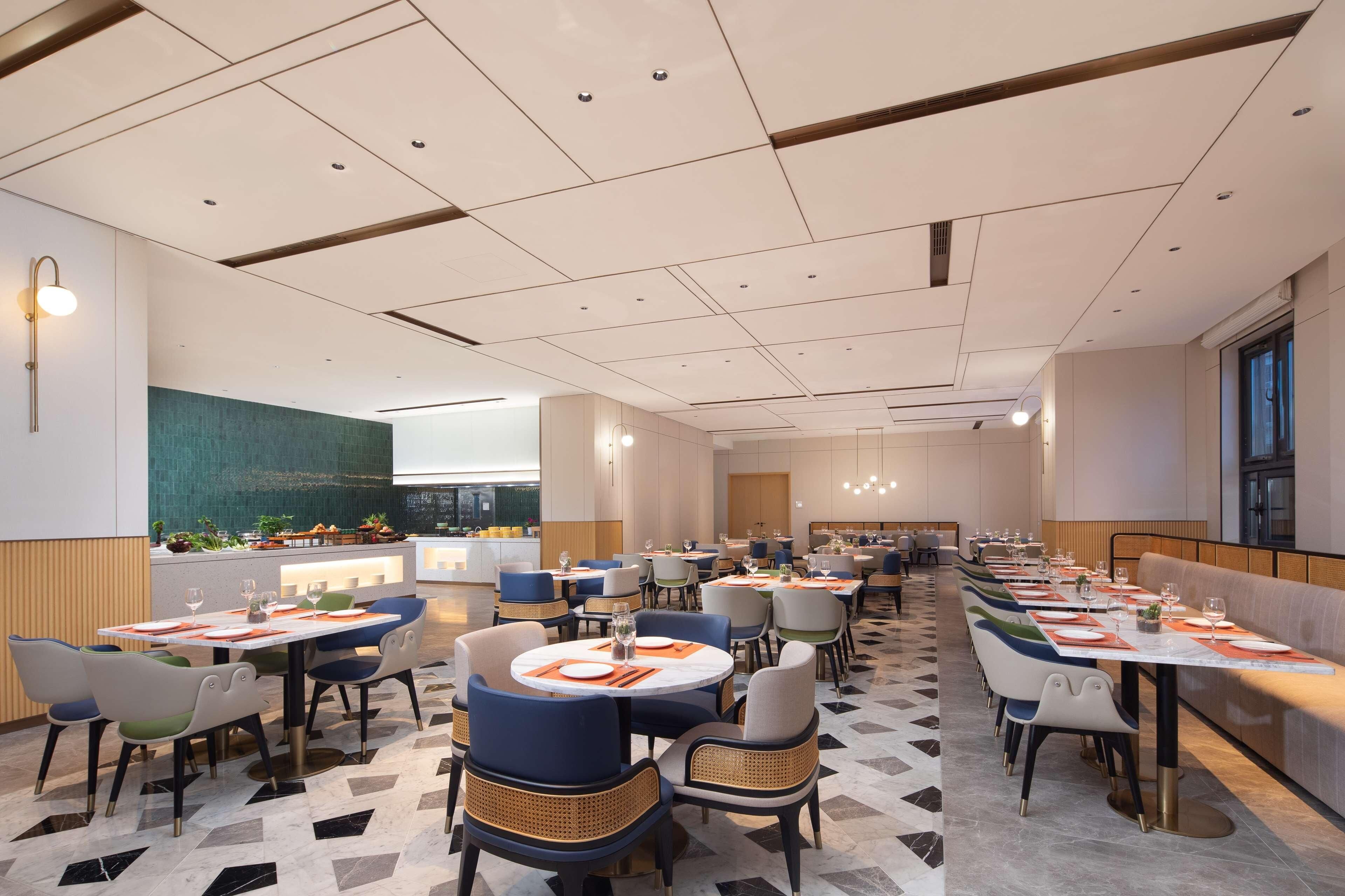 A spacious restaurant with multiple dining tables and chairs, a modern ceiling design, and a view of the kitchen area.