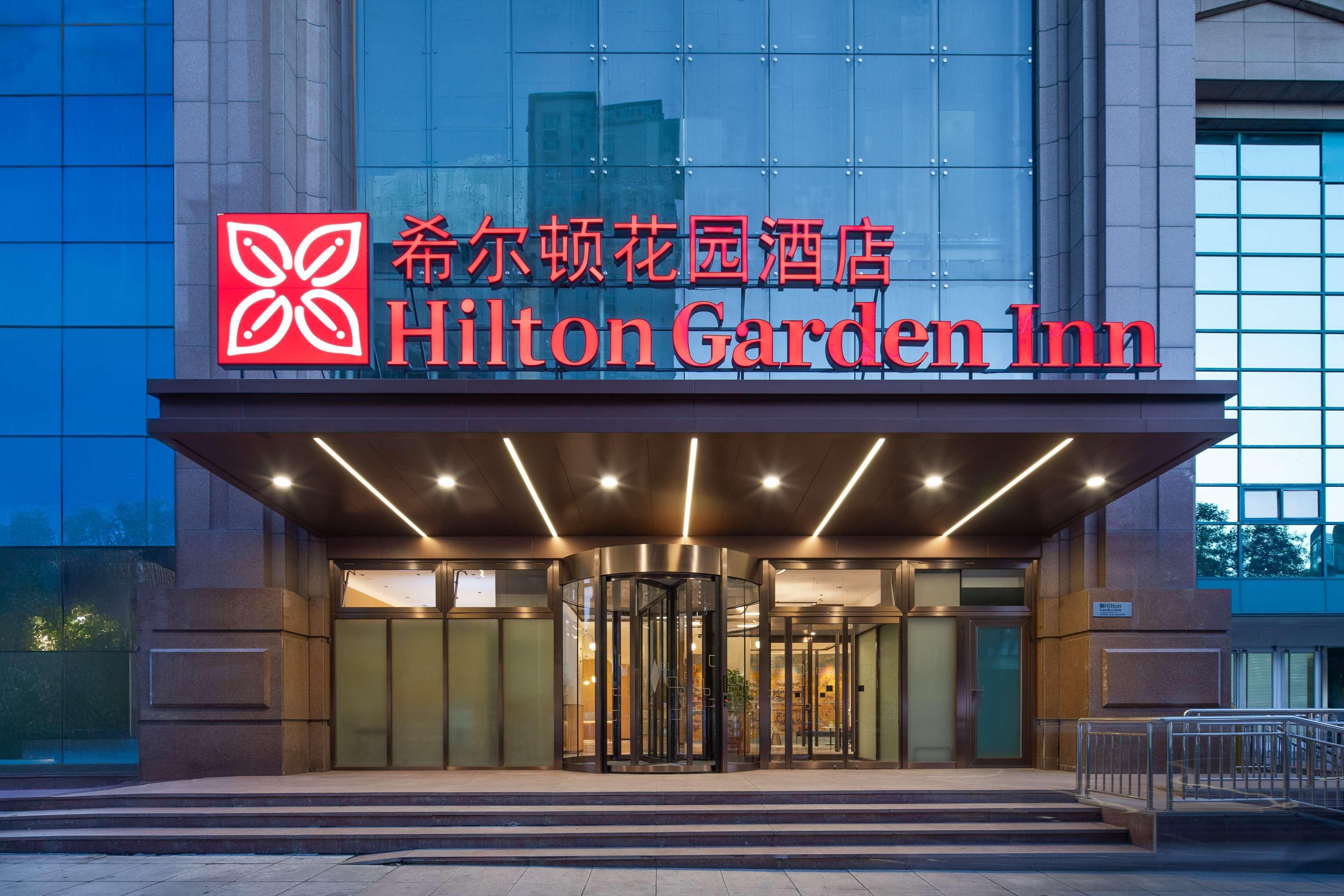 The exterior of the Hilton Garden Inn with a modern design, featuring a prominent entrance with revolving doors and a glass facade.