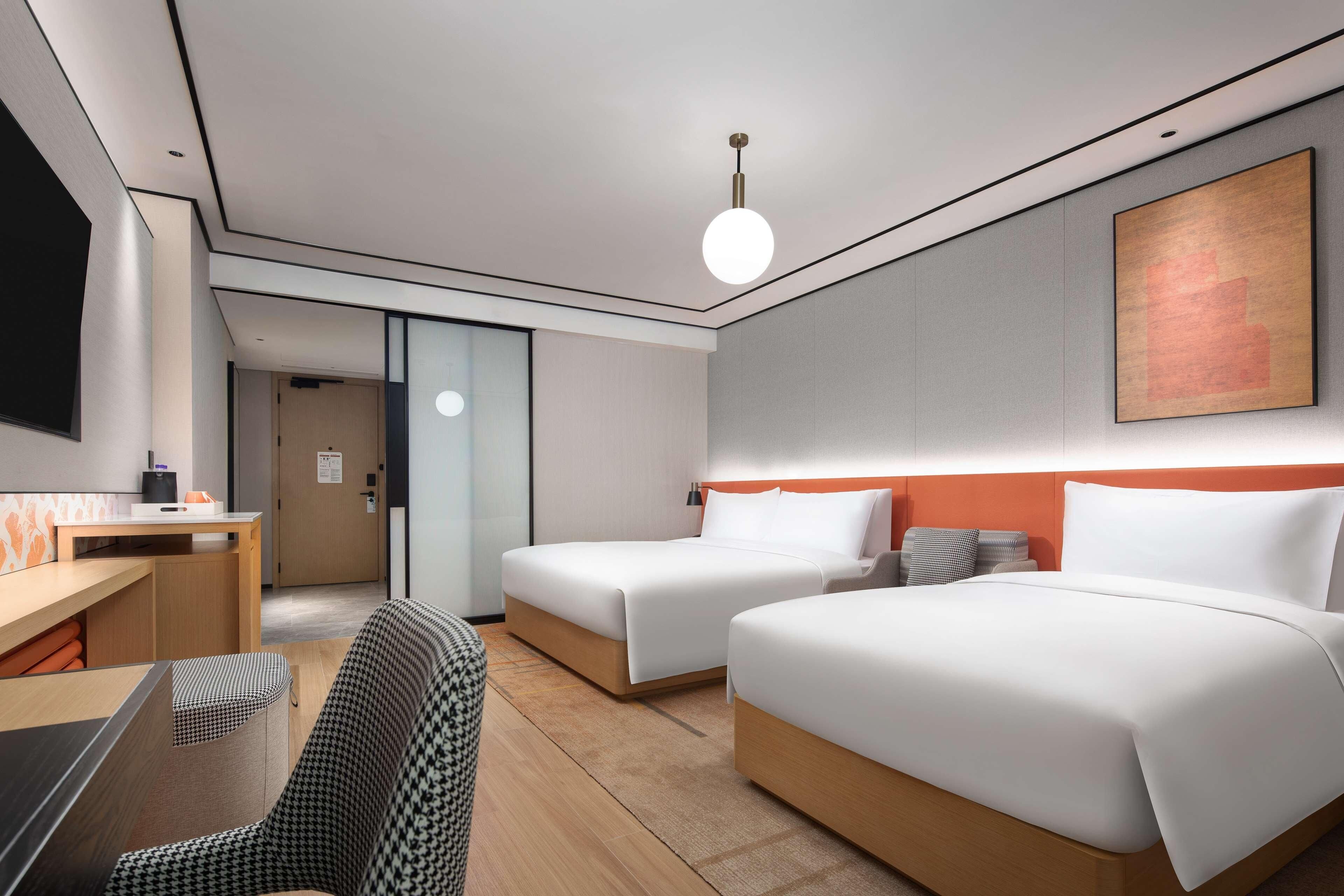 Ett modernt hotellrum med två sängar, ett skrivbord och en stol.