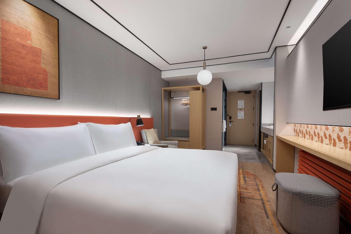 Ein Hotelzimmer mit einem großen Bett, einem Schreibtisch, einem Stuhl, einem Kleiderschrank und einem an der Wand montierten Fernseher.