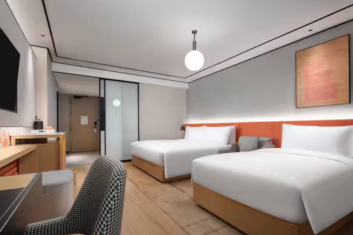 Ein Hotelzimmer mit zwei Betten, einem Schreibtisch, einem Sessel und einem großen Gemälde an der Wand.