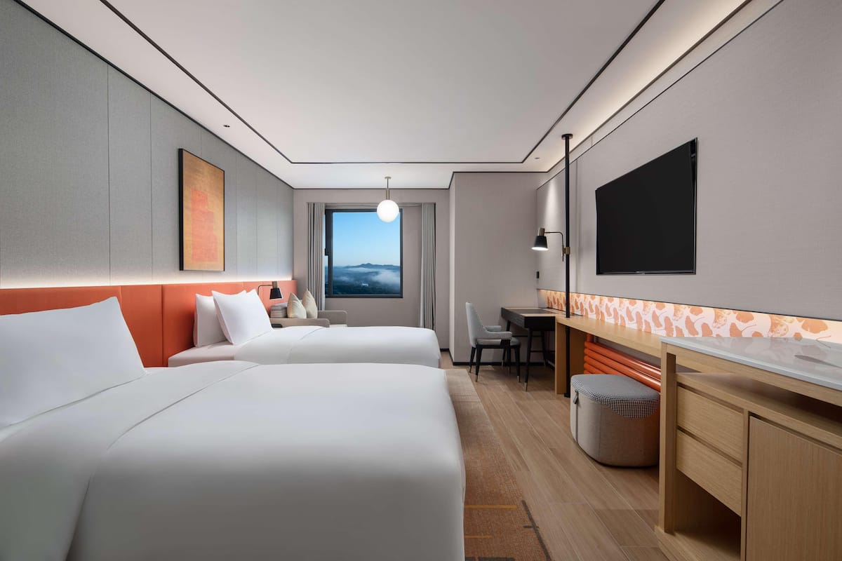 Ein Hotelzimmer mit zwei Betten, einem Schreibtisch, einem Fernseher und Blick zum Himmel.