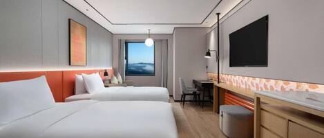 A modern hotel room with two beds, a desk, a TV, and a view of the sky.