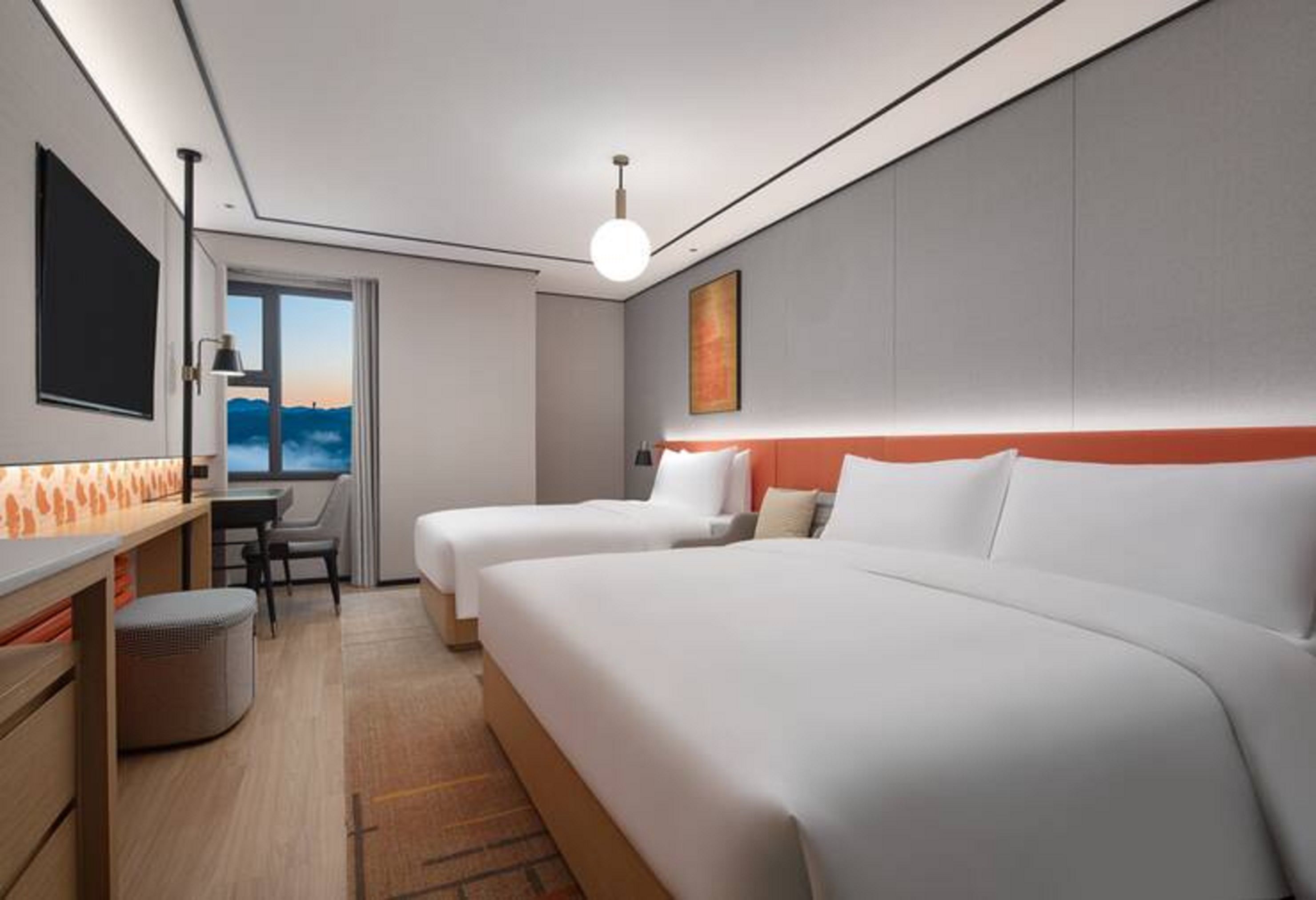 A hotel room with two beds, a desk, a chair, and a TV.