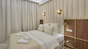 Camera d'albergo con un letto grande, tende beige, due luci a parete e un pannello in legno sulla parete destra.