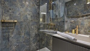 Un bagno moderno con pareti in marmo, cabina doccia in vetro e un vanitoio con dettagli dorati.