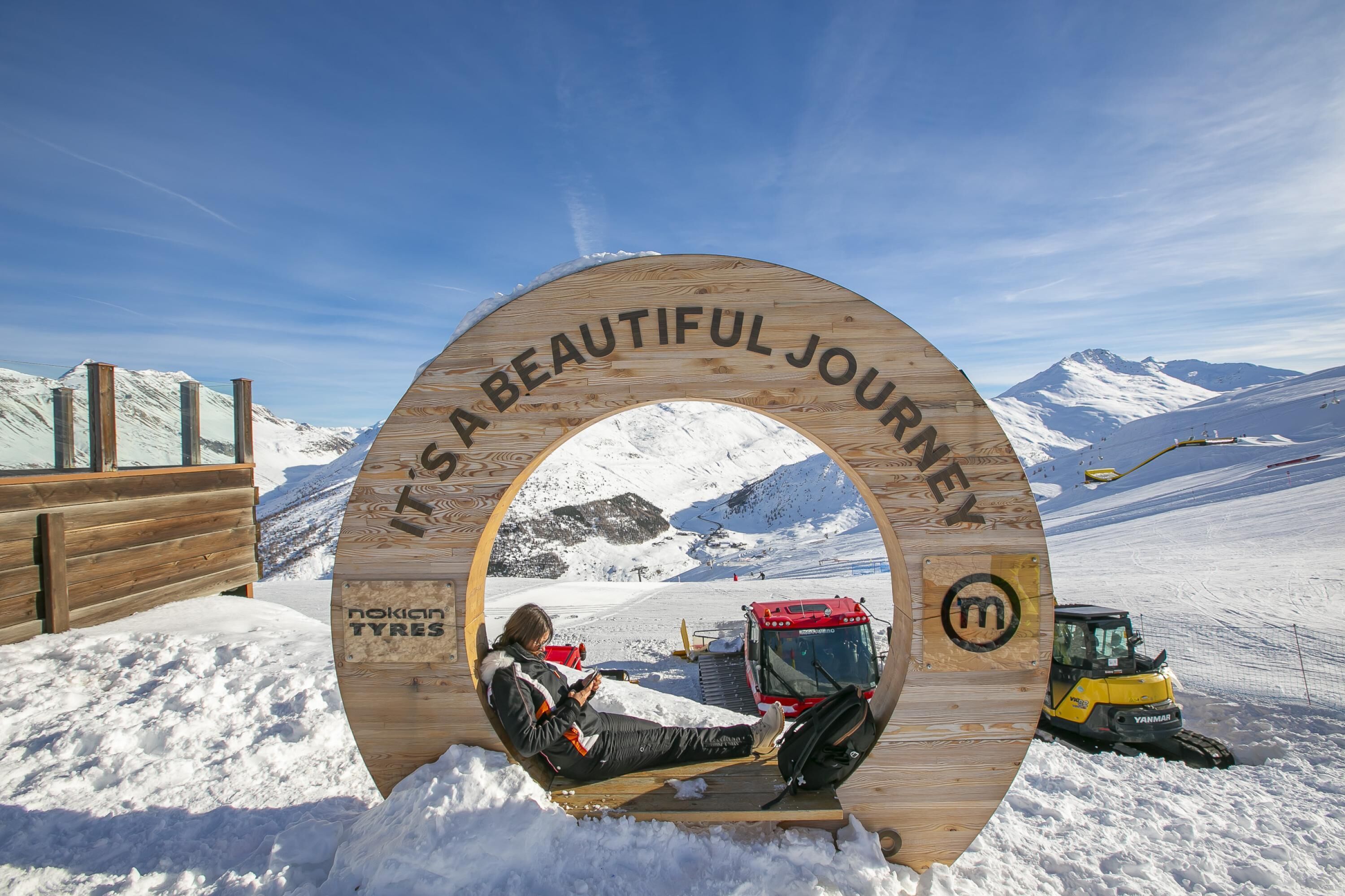 Une enseigne en bois portant l’inscription « C’est un magnifique voyage » et le nom « Nokian Tyres », le tout dans un paysage montagneux enneigé.