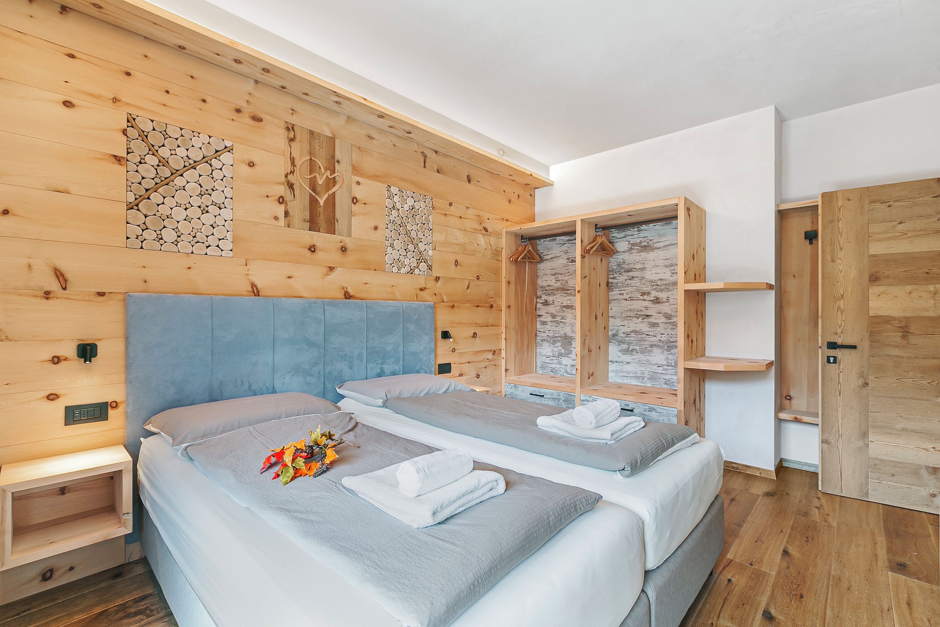 A room with two beds, wooden walls, a wooden wardrobe, and a small shelf.