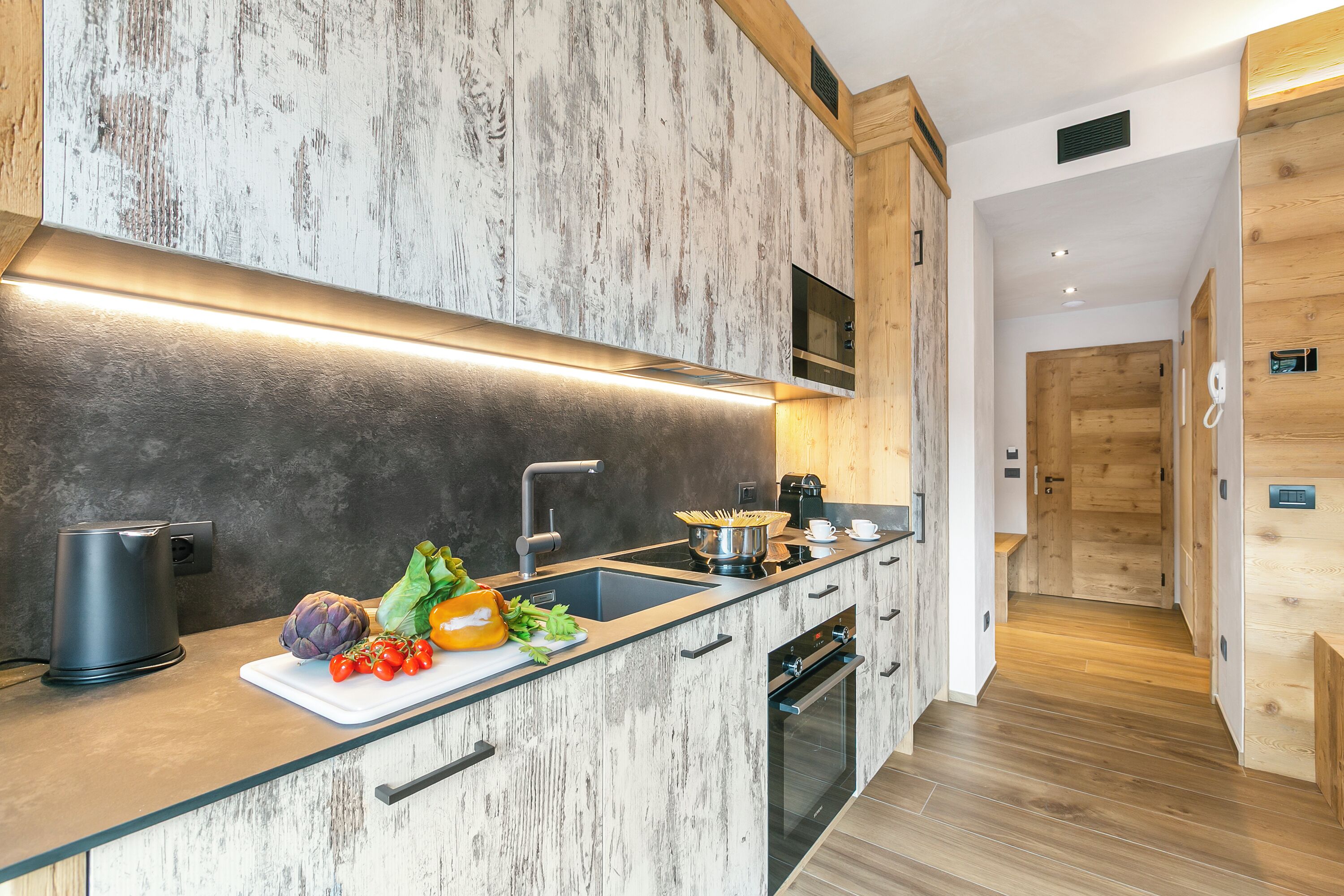 A modern kitchen with a wooden backsplash, a built-in oven, and a countertop with fresh vegetables.