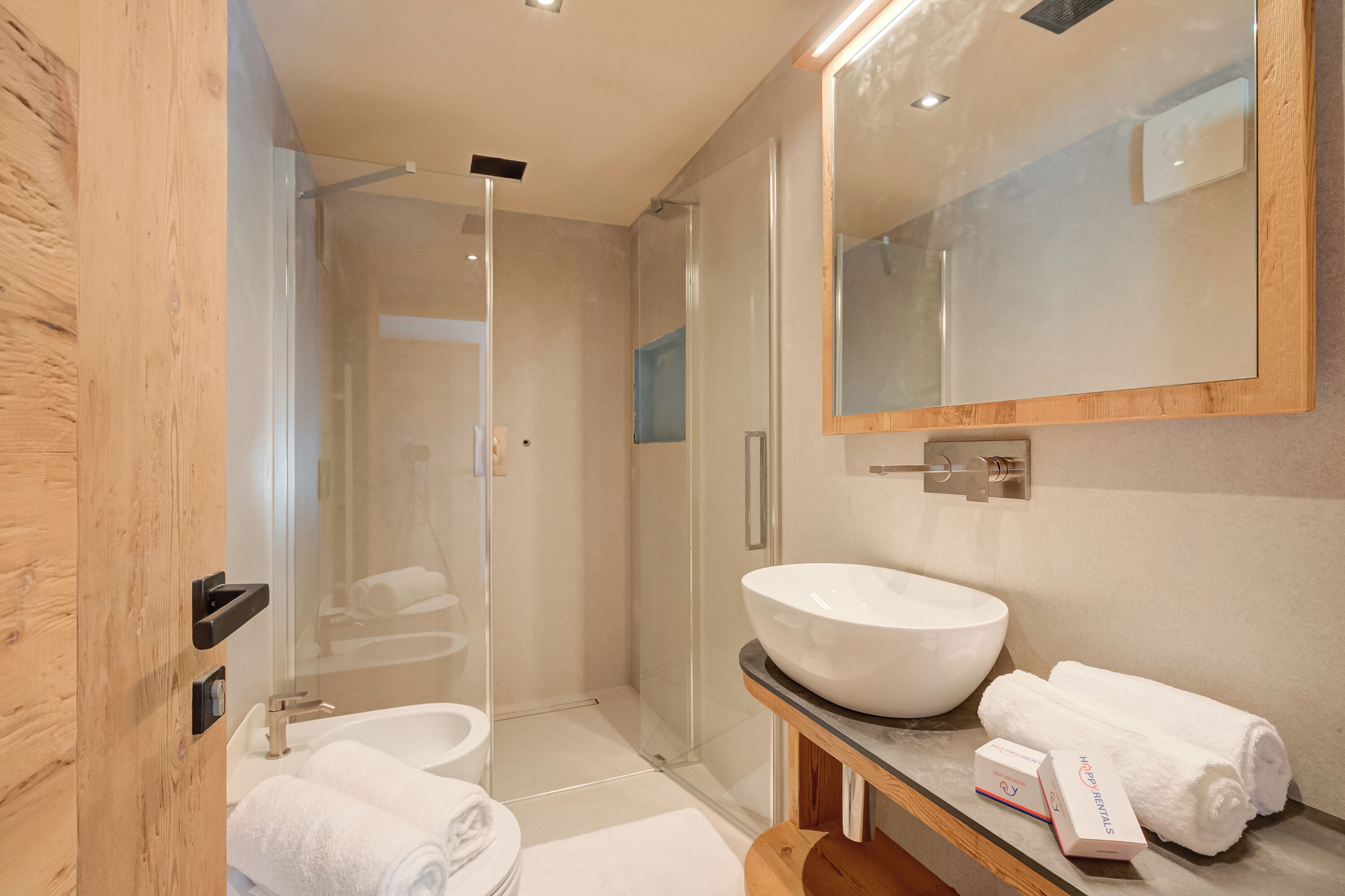 A modern bathroom with a glass-enclosed shower, a large white sink, and a wooden vanity.