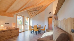 A spacious room with a wooden ceiling, a dining area with orange chairs, a sofa, and a wooden cabinet. - Cuore Alpino (Livigno)