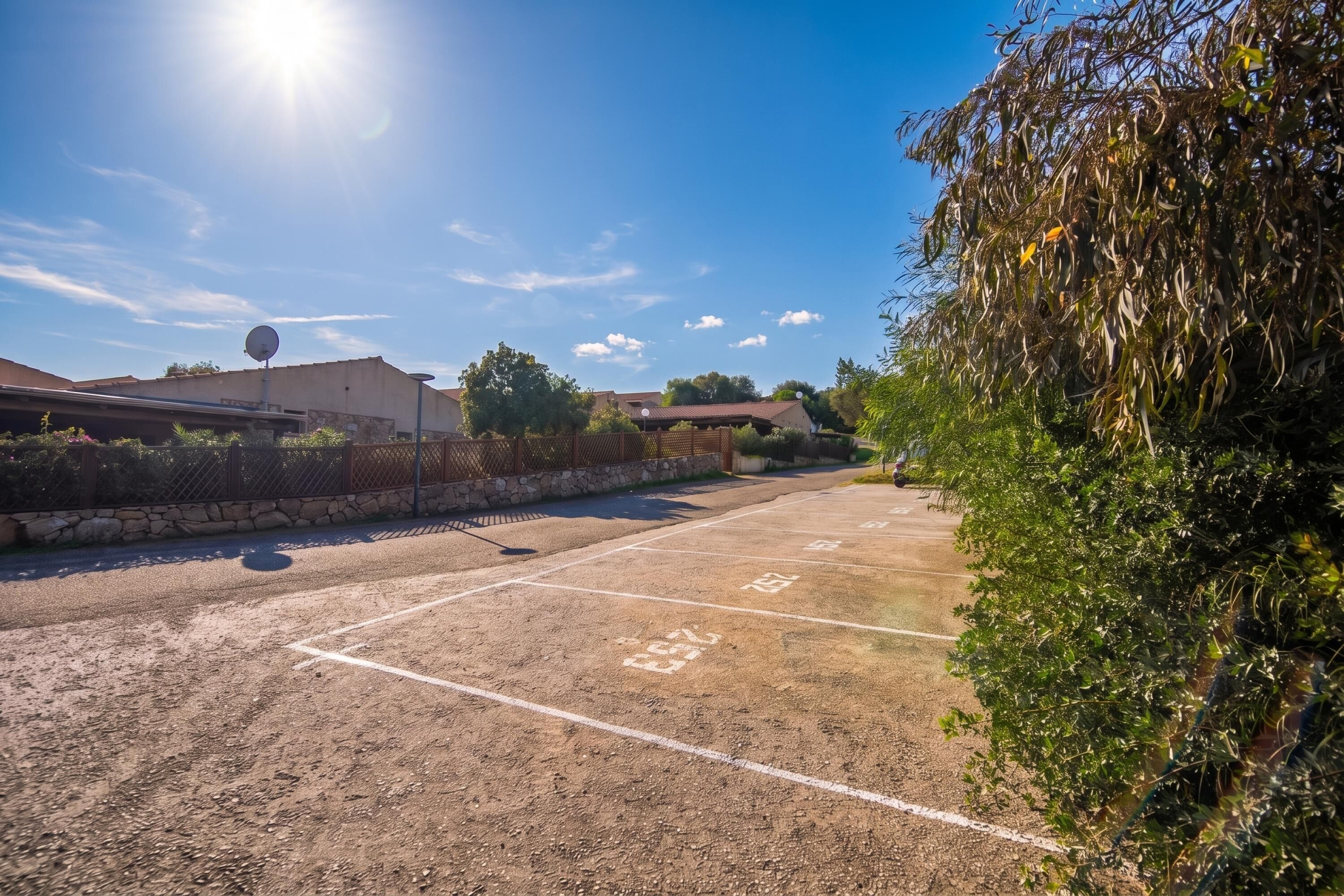 A parking lot with marked spaces, a stone wall, and a fence.