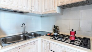 A kitchen with wooden cabinets, a stainless steel sink, a gas stove, and a coffee maker. - Sandy Bear Guesthouse (Palau)