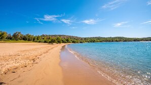 Une plage avec un ciel dégagé, une eau calme et un paysage vallonné en arrière-plan.