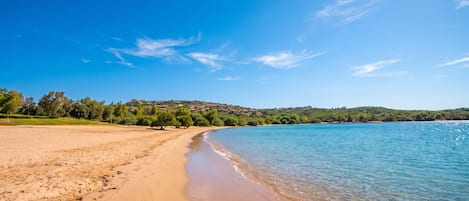 Una playa con cielo despejado, agua tranquila y un paisaje montañoso al fondo.