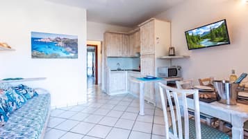 Una cocina moderna con gabinetes blancos, una mesa de comedor con sillas y un televisor montado en la pared.