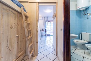 A bathroom with a toilet, a sink, and a shower. There is a wooden wardrobe with a ladder in the adjacent room. - Sandy Bear Guesthouse (Palau)