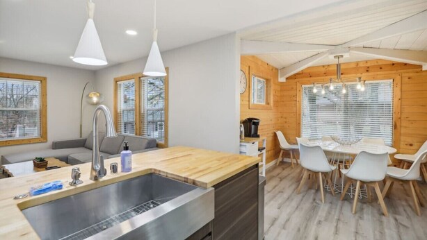 A modern kitchen with a wooden countertop and stainless steel sink, a dining area with a white table and chairs, and a wooden ceiling with exposed beams. - Hines Terrace Retreat - Hot Tub & Firepit (Wisconsin Dells)