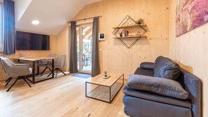 A modern living room with a wooden floor, a grey sofa, a coffee table, and a dining area with a table and chairs. - Ferienwohnung mit 1 Schlafzimmer & Sauna (Oberwölz)