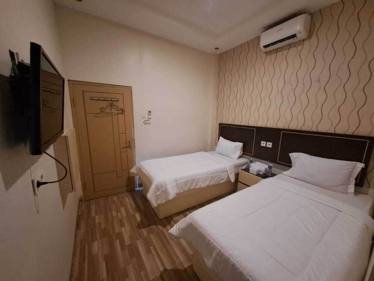 A hotel room with two beds, a wardrobe, a TV, and an air conditioning unit.