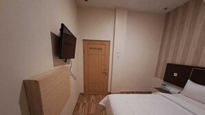 Ein Hotelzimmer mit hölzernem Kopfteil, einem Bett mit weißer Bettwäsche, einem an der Wand montierten Fernseher und einer Holztür.