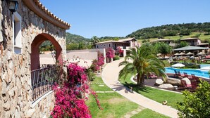 A resort with a stone archway, a swimming pool area with lounge chairs, and a view of the surrounding hills. - Two-room Apartment in a Complex (Villasimius)