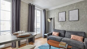 A modern living room with a grey sofa, a round coffee table, and a dining table set with plates and glasses. - Apartment Center of Paris (Paris)