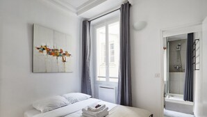 A hotel room with a bed, a window with curtains, a shower area, and a wall-mounted artwork. - Apartment Center of Paris (Paris)