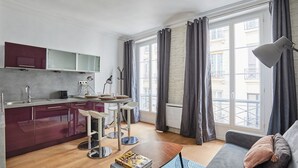 A modern apartment with a kitchen, dining area, and living room. It features a large window with curtains, a sofa, and a coffee table. - Apartment Center of Paris (Paris)